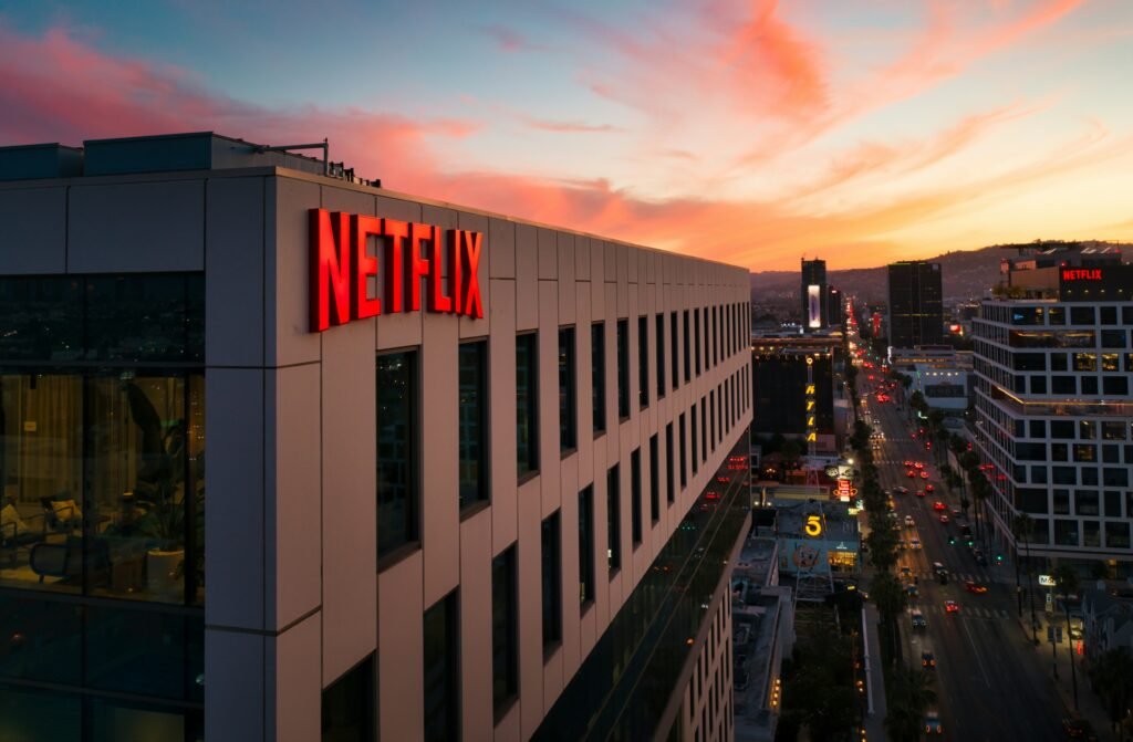 Сградата на Netflix с осветено лого при залез слънце, гледка към градска улица и небостъргачи в Лос Анджелис, САЩ