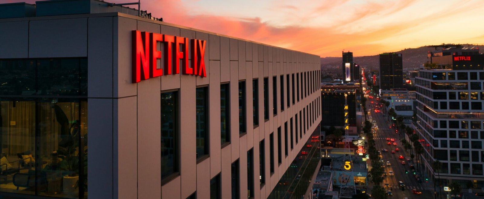 Сградата на Netflix с осветено лого при залез слънце, гледка към градска улица и небостъргачи в Лос Анджелис, САЩ