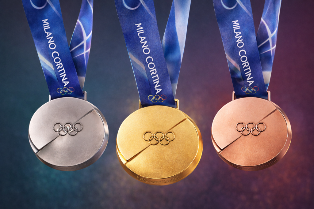 Златен, сребърен и бронзов олимпийски медал за Зимните олимпийски игри Милано–Кортина 2026, окачени на сини ленти с олимпийските кръгове.